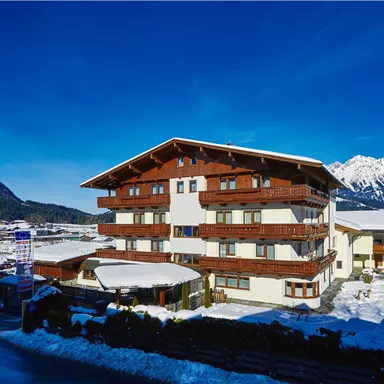 Ein charmantes Gebäude im Alpenstil umgeben von Schnee und Bergen. Der Himmel ist klar und blau, was eine einladende Atmosphäre schafft.