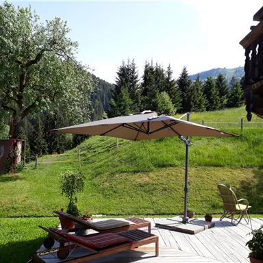 A beautiful garden with a terrace, loungers, and a parasol. In the background, green meadows and trees can be seen.