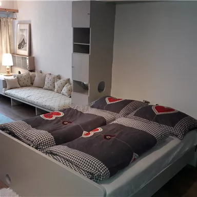 A modern bedroom with a double bed and lovely bedding. Next to the bed is a cozy couch and a table with a lamp.