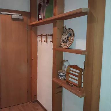 A cozy hallway with a wooden shelf, a door, and decorative elements. On the wall hang coats and a decorated plate.