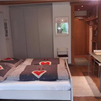 A cozy bedroom with a double bed and a neutral color palette. The room features a table and shelves that provide additional functionality.