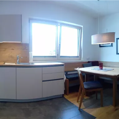 Eine moderne Küche mit einer gemütlichen Essecke. Helle Farben und viel natürliches Licht schaffen eine einladende Atmosphäre.