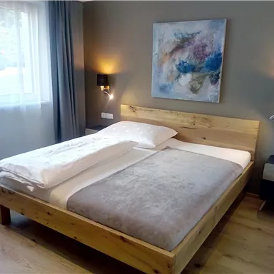 Ein modernes Schlafzimmer mit einem Holzbett und einem Gemälde an der Wand. Die Räume sind hell und freundlich mit Tageslicht und stilvollem Dekor.