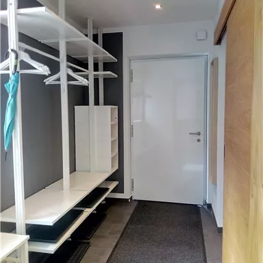 Ein heller Flur mit modernen Ablagemöglichkeiten und einem weißen Tür. Die Wände sind in neutralen Farben gehalten, was eine einladende Atmosphäre schafft.