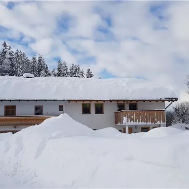 A snow-covered house surrounded by tall snow mountains. The sky is clear with some clouds.