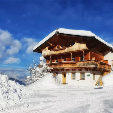 Ein gemütliches Holzhaus im Winter, umgeben von viel Schnee. Der Himmel ist klar mit einigen Wolken.