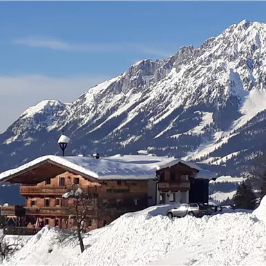 A charming wooden house in the snow with impressive mountains in the background. The landscape is wintery and peaceful.
