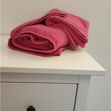 Ein Stapel rosa Handtücher liegt auf einer weißen Kommode. Die Handtücher sind ordentlich aufgerollt und wirken frisch und sauber.