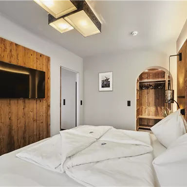 Ein modernes Hotelzimmer mit einem gemütlichen Bett und rustikalen Holzakzenten. Der Raum ist hell und gut ausgestattet, mit einem Fernseher an der Wand.