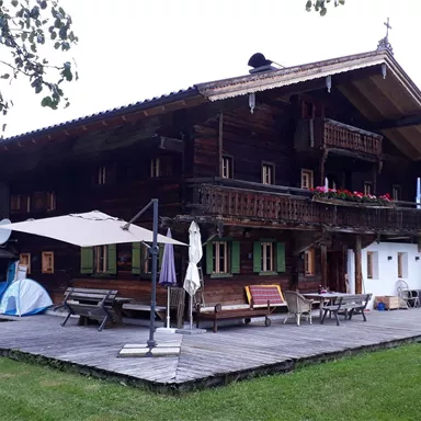 A traditional wooden house in a picturesque landscape. The large garden is equipped with wooden loungers and a sun umbrella.