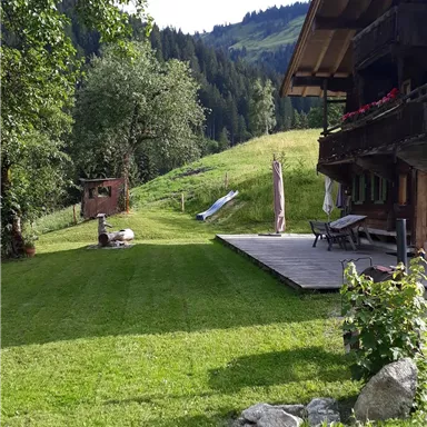 A beautiful garden with well-maintained lawn and a view of the mountains. In the background, there is a traditional wooden house.
