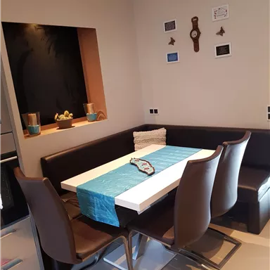 Ein moderner Essbereich mit einem Tisch und Stühlen in erdigen Farbtönen. Der Tisch ist mit einer blauen Tischdecke dekoriert und befindet sich in einer gemütlichen Ecke.