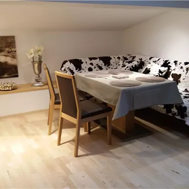 Ein gemütlicher Essbereich mit einem Tisch und Holzstühlen. Die Couch hat ein Schwarz-Weiß-Muster, und der Raum ist gut beleuchtet.