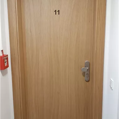 A simple wooden front door with the number 11. The door is light-colored and has a modern door handle.