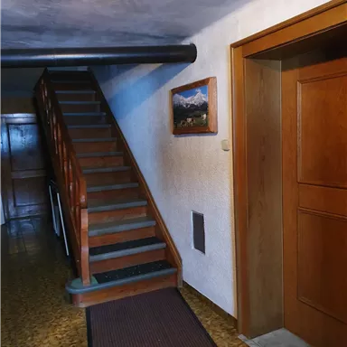 Ein einladender Flur mit einer Holztreppe und einem gemalten Landschaftsbild an der Wand. Die Wände sind hell und der Boden ist mit einem Teppich ausgelegt.