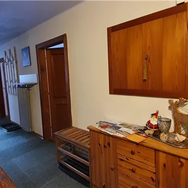 Ein gemütlicher Flur mit Holzvertäfelungen und einer Holzkommode. An der Wand hängen Skier, und auf dem Tisch stehen verschiedene Dekorationen.