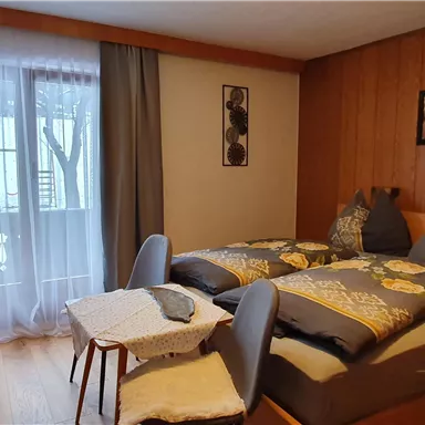 Ein gemütliches Schlafzimmer mit zwei Betten, einem kleinen Tisch und einem Blick auf den Balkon. Die Wände sind aus Holz und es gibt Vorhänge, die Licht durchlassen.