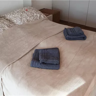 A cozy bedroom with a bed and clean bed linens. On the blanket lie two folded towels.