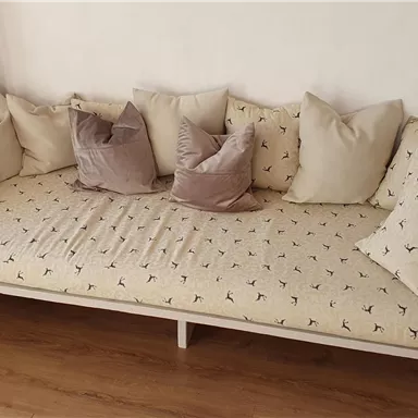 A cozy bench with many cushions. The cover has an attractive pattern and the surroundings appear bright and inviting.