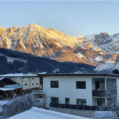 A picturesque winter landscape with snow-covered mountains in the background. In the foreground stands a modern residential house.