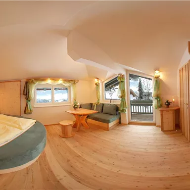 A comfortable room with a double bed and a cozy seating area. Large windows provide plenty of daylight and a view outside.