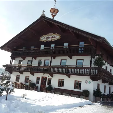 Ein traditionelles Holzhaus im alpine Stil, umgeben von Schnee. Es hat große Balkone und eine freundliche Beschilderung.