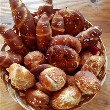 A basket full of fresh rolls and pretzels. The baked goods are golden brown and shiny.