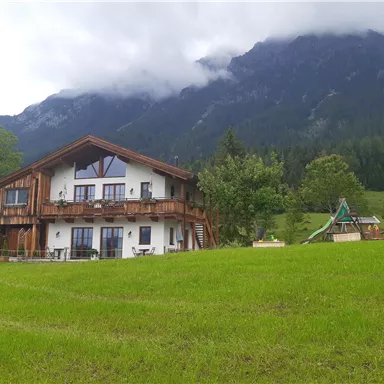 Eine malerische Almhütte umgeben von grünen Wiesen und majestätischen Bergen. Der Himmel ist bewölkt, was eine gemütliche Atmosphäre schafft.