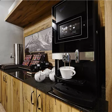 Eine moderne Kaffeeautomaten-Ecke mit Holzregalen. Es sind Kaffeetassen und Zubehör auf der Arbeitsfläche arrangiert.