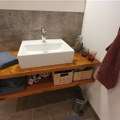 A modern sink on a wooden shelf in a bathroom. Towels and toiletries are neatly arranged.