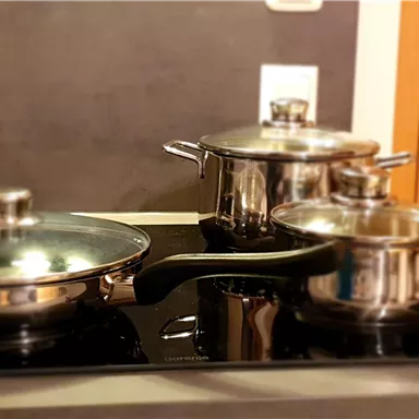 A modern kitchen with a cooking hob and shiny cookware. Two pots and a pan await the preparation of meals.