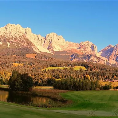 An impressive mountain landscape with a wide meadow and clear sky. The sun illuminates the peaks and creates a picturesque atmosphere.