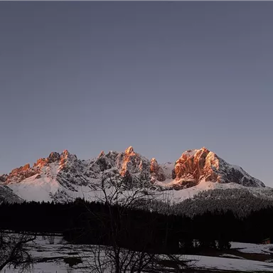 Eine beeindruckende Berglandschaft mit schneebedeckten Gipfeln und einem sanften Sonnenuntergang. Der Himmel ist klar und die Umgebung ist ruhig.