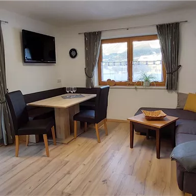 Ein gemütlicher Wohnraum mit einem Sofa, einem Tisch und Stühlen. Große Fenster bieten einen Blick auf die verschneite Landschaft.