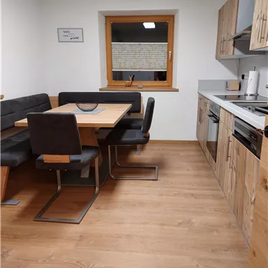 A modern kitchen with a dining table and bench. The room has light wooden paneling and a window that lets in natural light.