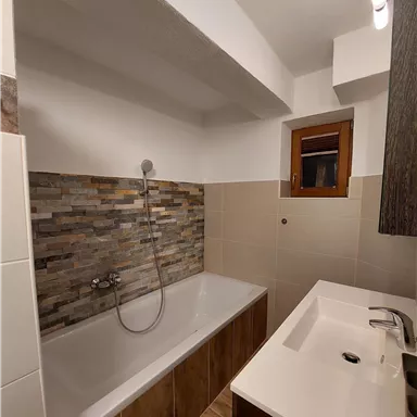 A modern bathroom with a bathtub and a sink. The walls are partially decorated with decorative tiles.