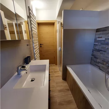 A modern bathroom with a sink, a bathtub, and elegant wood and tile elements. Abundant light shines through the space, creating an inviting atmosphere.
