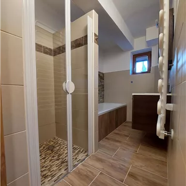 A modern bathroom with a shower and bathtub. It features a bright color scheme and windows for natural light.