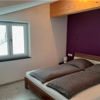 Ein gemütliches Schlafzimmer mit einem Doppelbett und künstlerischer Wandfarbe. Das Fenster bietet einen Blick auf die Schneelandschaft draußen.