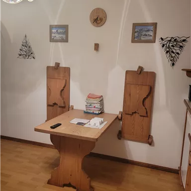 Ein rustikaler Essbereich mit einem Holztisch und zwei gepolsterten Stühlen. An der Wand hängen Bilder und dekorative Elemente.