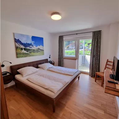 Ein einfaches Schlafzimmer mit zwei Betten und einem Holztisch. Große Fenster bieten Blick auf die Natur draußen.