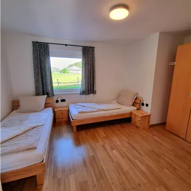 Ein einfaches Zimmer mit zwei Einzelbetten und Holzfussboden. Das Fenster bietet einen Blick ins Grüne.