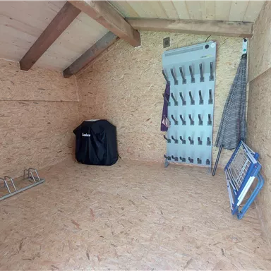 An empty room with wooden-paneled walls and a high ceiling. On the left side, there are some hanging possibilities and a grill.