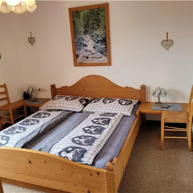 Ein gemütliches Schlafzimmer mit einem großen Holzbett und zwei kleinen Tischen. An den Wänden hängen Bilder von Landschaften.
