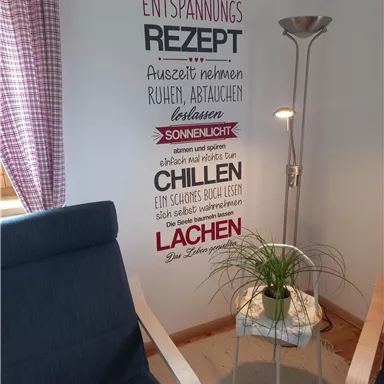 Ein gemütlicher Raum mit zwei Sessel, einer Stehlampe und einer Wandgestaltung, die Entspannungstipps bietet. Die Atmosphäre ist einladend und beruhigend.