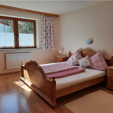 Ein gemütliches Schlafzimmer mit einem großen Bett und Holzkommoden. Die Fenster lassen viel Tageslicht herein und sorgen für eine helle Atmosphäre.