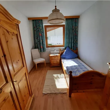Ein gemütliches Schlafzimmer mit Holzschränken und einem Einzelbett. Das Zimmer hat einen großen Fenster mit Vorhängen und einen kleinen Nachttisch.