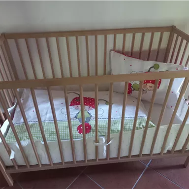 Ein Holz-Kinderbett mit einem gepolsterten Kissen und einer Decke. Die Bettwäsche hat ein fröhliches Erdbeer-Muster.