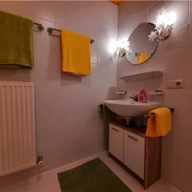 Ein modernes Badezimmer mit einem Waschbecken und einem runden Spiegel. Bunte Handtücher in Gelb und Grün verleihen dem Raum Farbe.