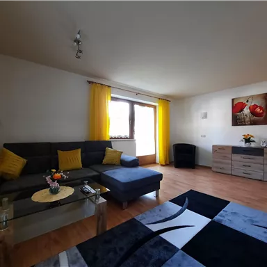 Ein modernes Wohnzimmer mit einem grauen Sofa und gelben Vorhängen. Der Raum hat einen Holzboden und einen stilvollen Teppich sowie eine kleine Blumendekoration.